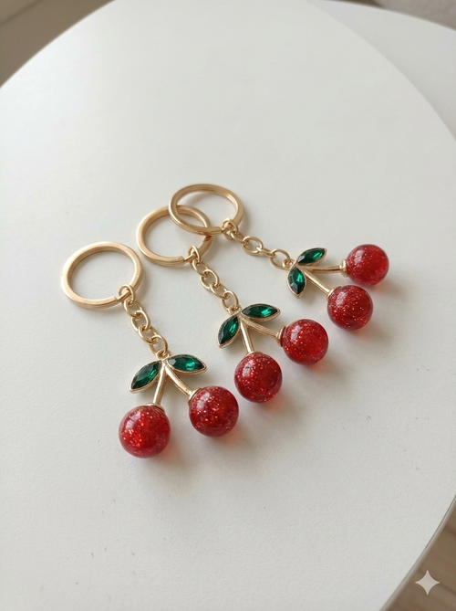 Three red crystal cherry keychains on white surface