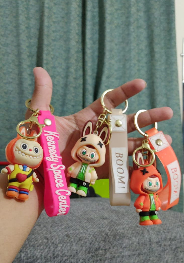 Three Labubu style figurine keychains with wrist straps held in hand