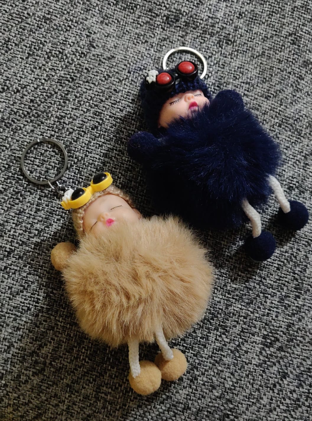 Navy blue and beige sleeping baby doll pom pom keychains on grey fabric